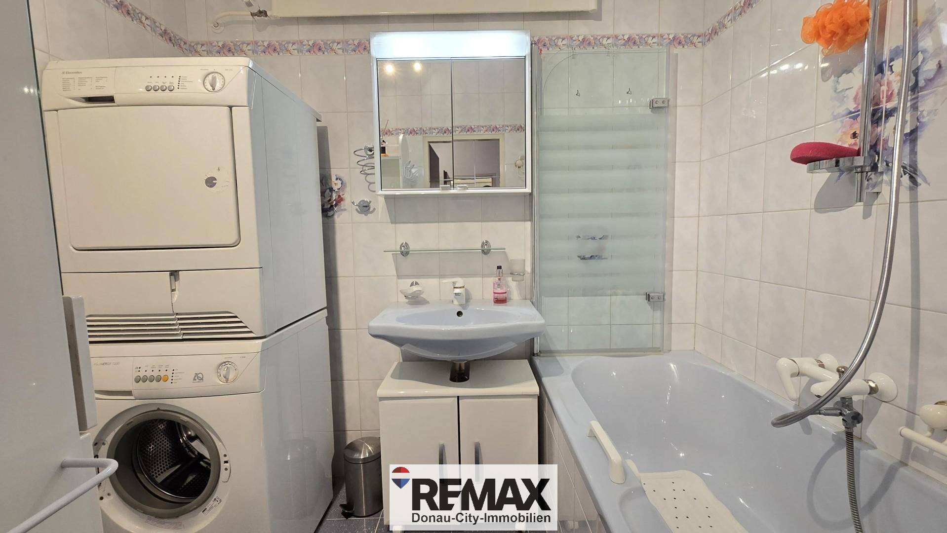 Badezimmer mit Badewanne, Waschbecken, Waschmaschine und Trockner, alles auf kleinem Raum.