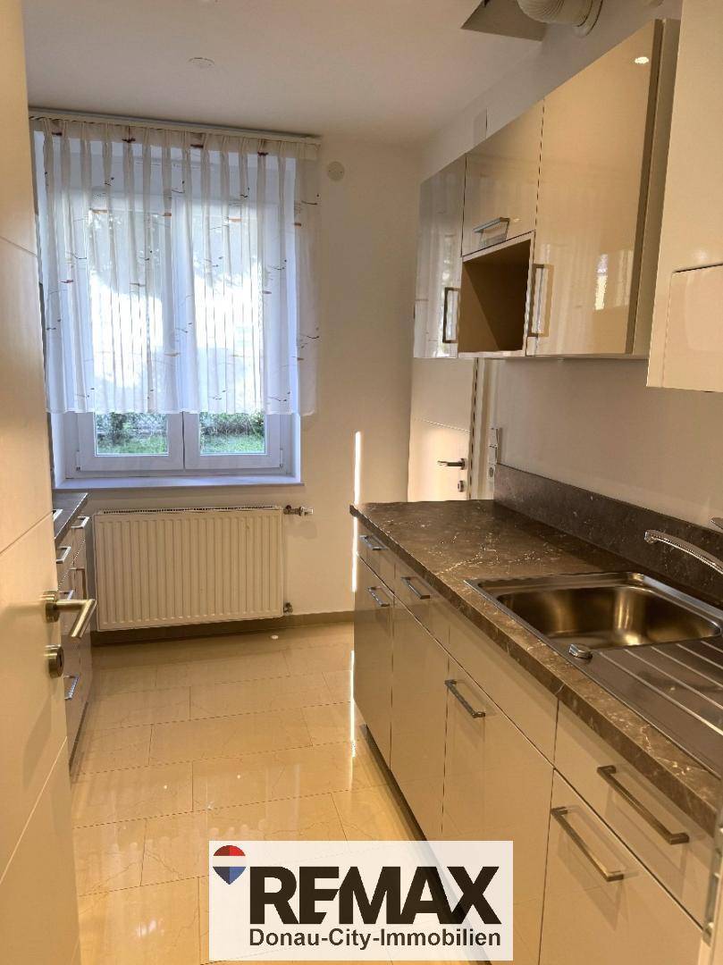 Moderne Küche mit Spülbecken, glänzenden Schränken und hellen Fliesenböden.