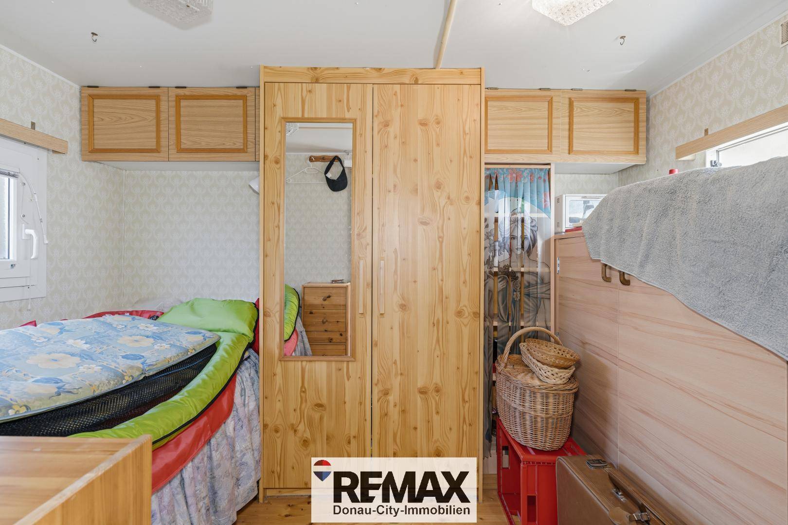 Schlafzimmer mit Holzkleiderschrank, Spiegel und praktischem Stauraum über dem Bett.
