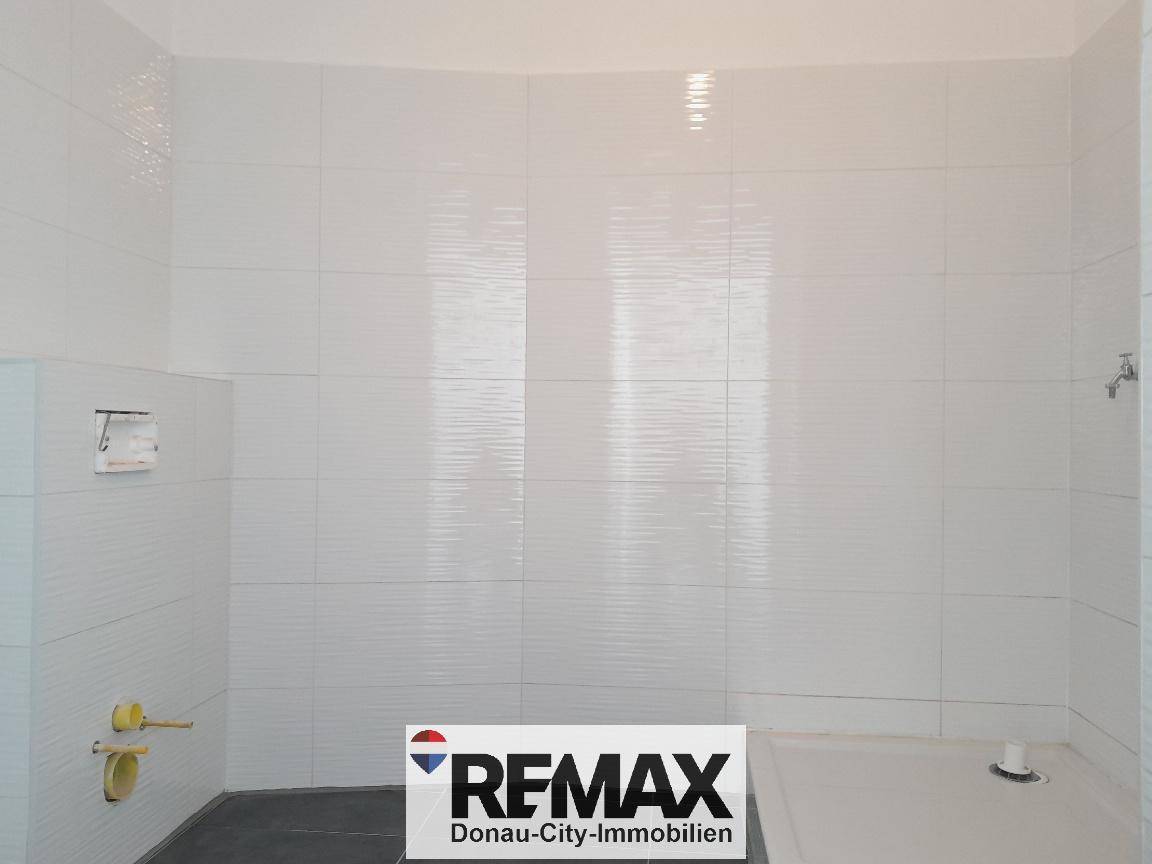 Modern gefliestes Badezimmer mit weißen Wandfliesen und vorbereitetem Duschbereich.