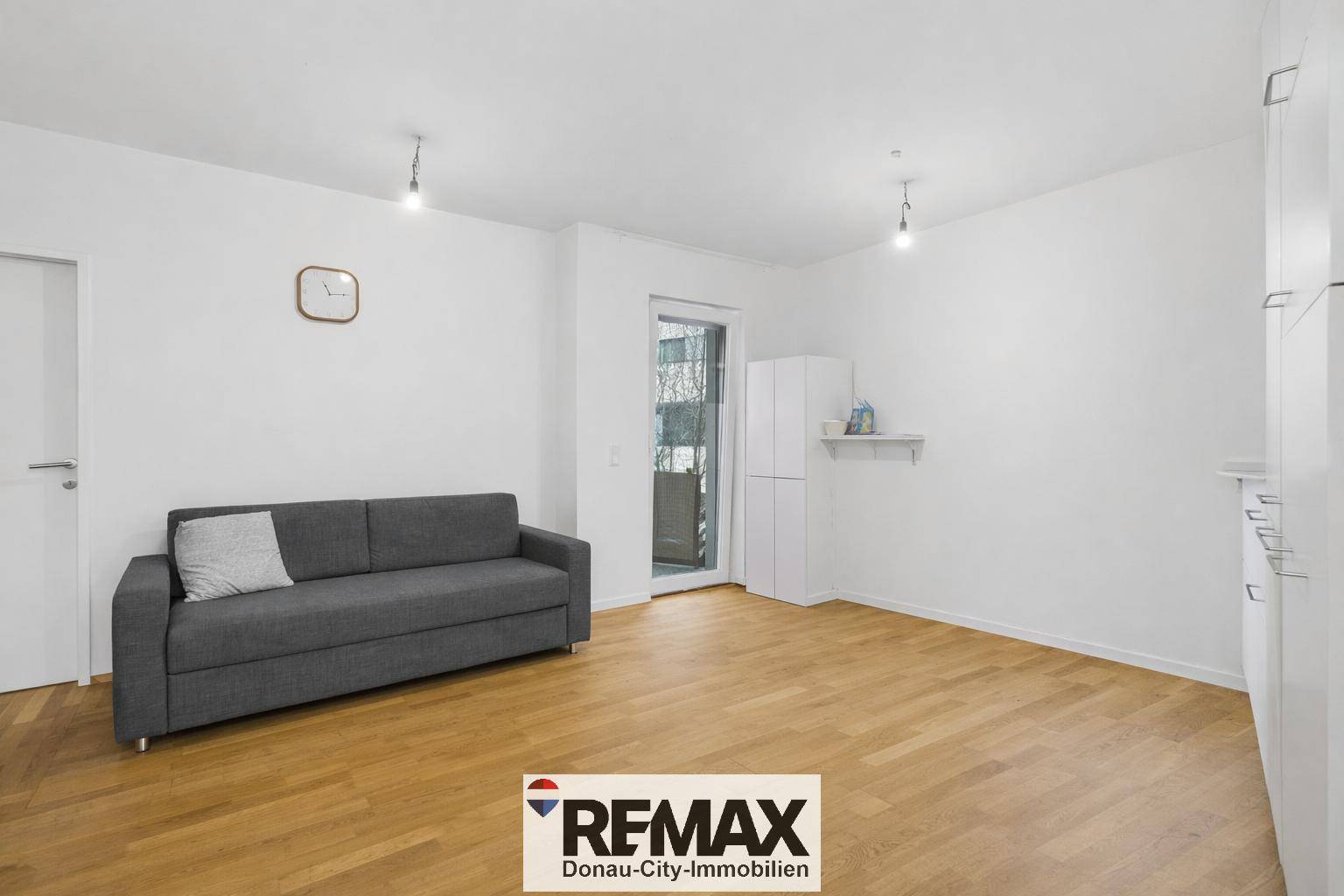 Helles Wohnzimmer mit Sofa, Holzboden und Zugang zu einem Balkon.
