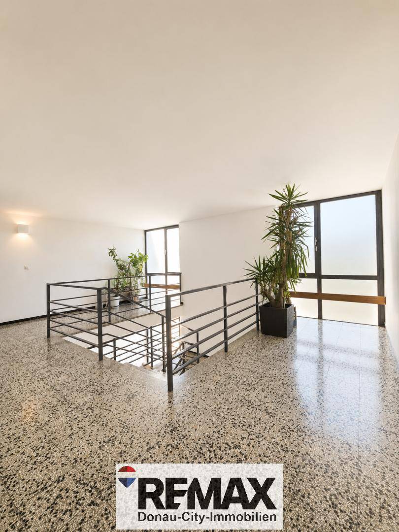 Heller Flur mit Treppenaufgang, großen Fenstern und Terrazzo-ähnlichem Bodenbelag.