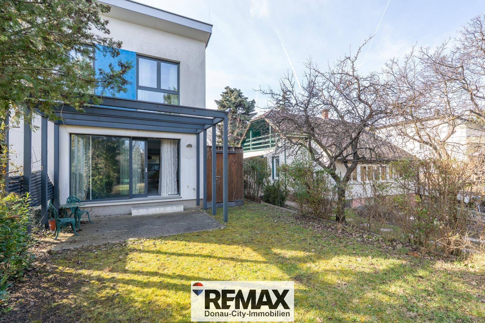 Hinterhof mit kleiner Terrasse, Rasenfläche und Bäumen, ideal zum Entspannen.