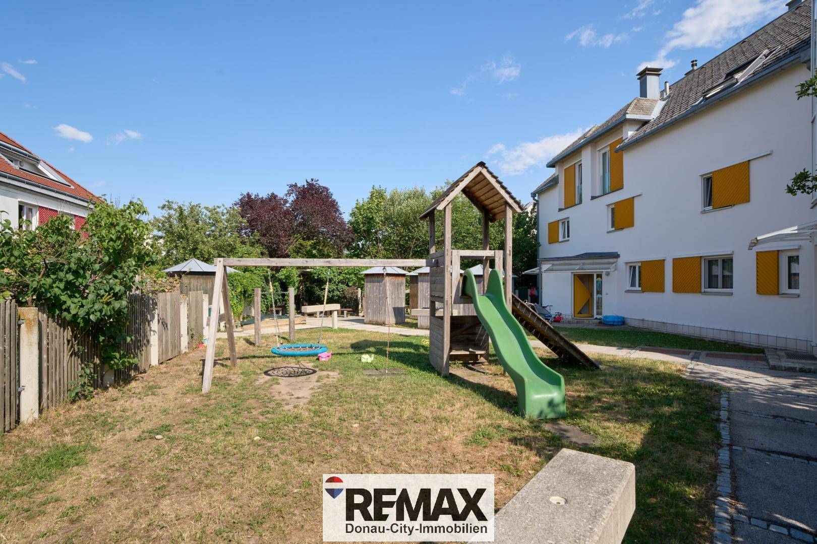 Gemeinschaftlicher Spielplatz mit Rutsche und Schaukeln, umgeben von Grünflächen.