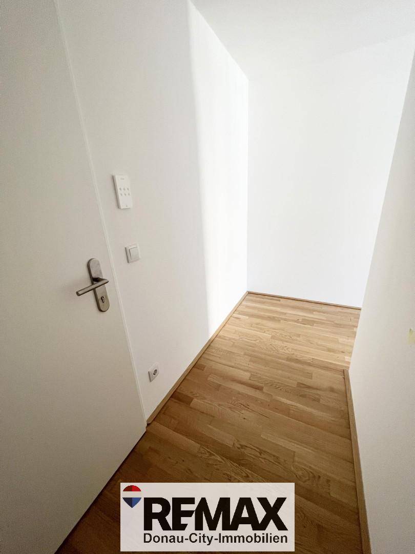 Heller Flur mit Holzboden und weißen Wänden, der zu weiteren Räumen führt.