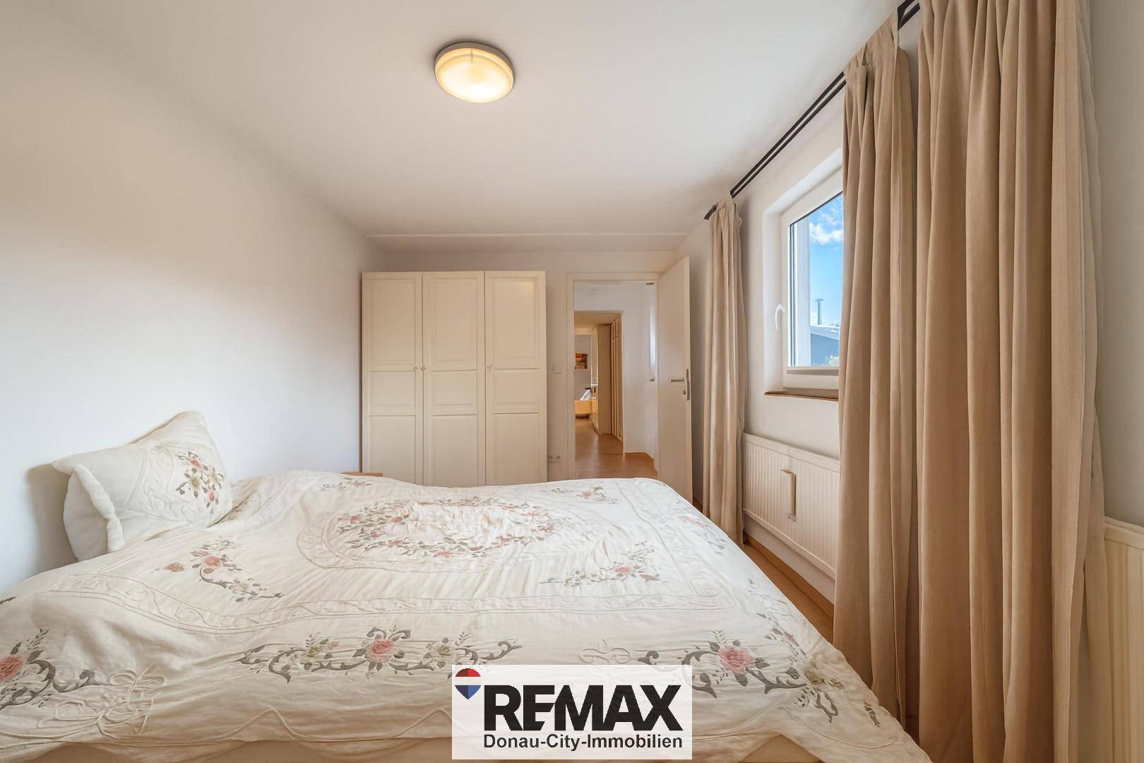 Schlafzimmer mit Bett, Kleiderschrank und Fenster mit Vorhängen.