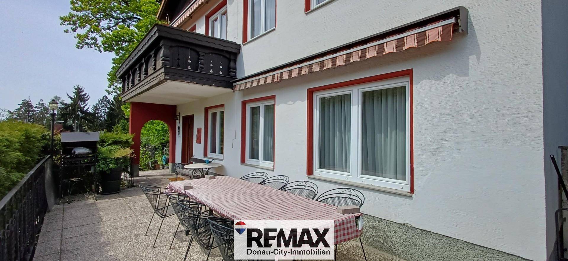 Große Terrasse mit Esstisch und Stühlen, darüber ein traditioneller Holzbalkon.