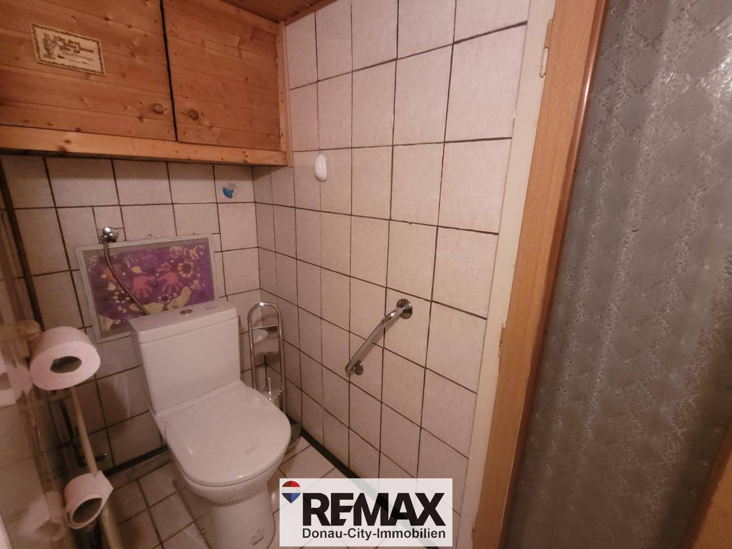 Separate Toilette mit Fliesen, WC, Haltegriff und Holzschränken.