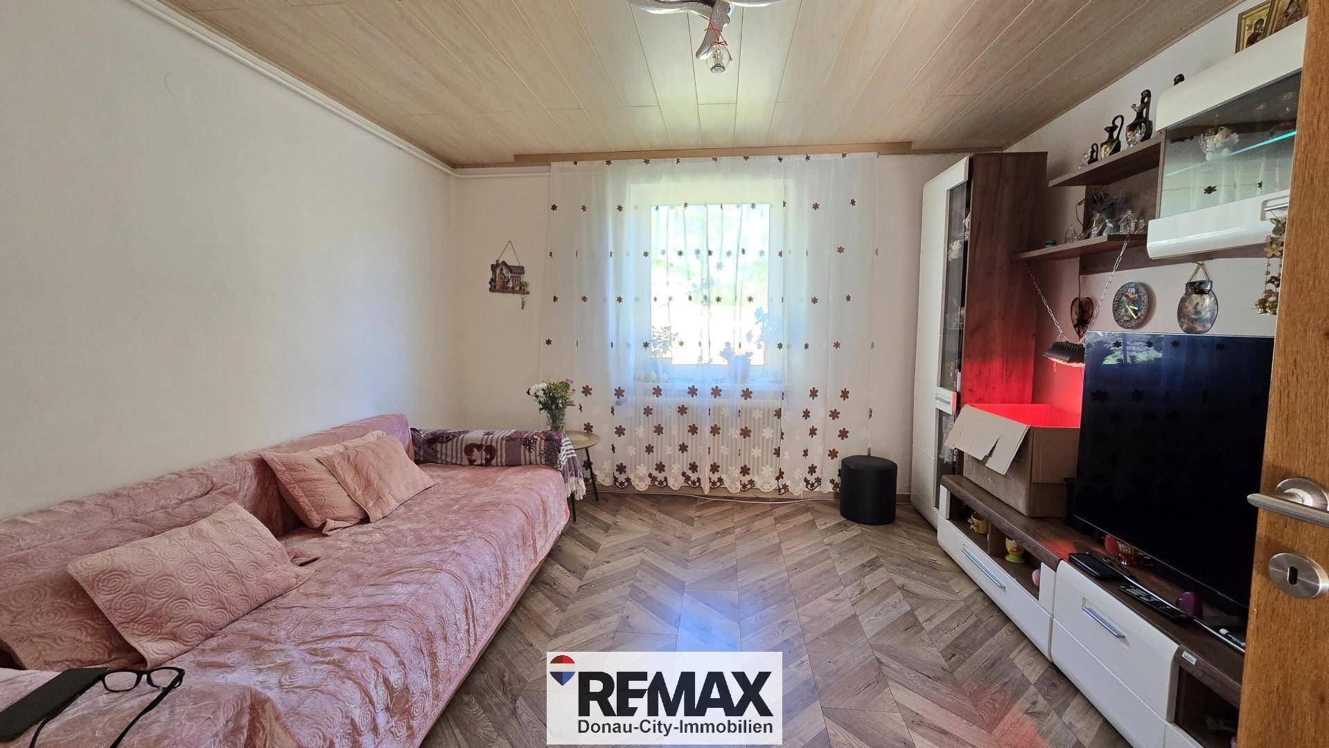 Gemütlicher Wohnraum mit Sofa, Fernseher und Holzdecke.