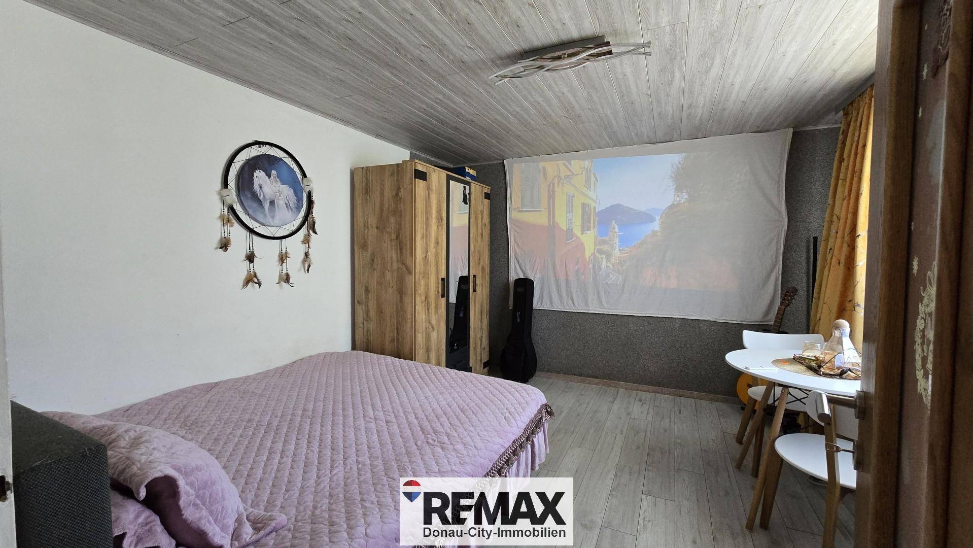 Schlafzimmer mit Bett, Kleiderschrank und Projektionsfläche für Unterhaltung.