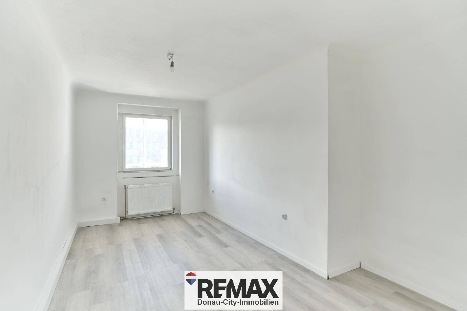 Helles Schlafzimmer mit Laminatboden und einem Fenster, bereit zur persönlichen Gestaltung.