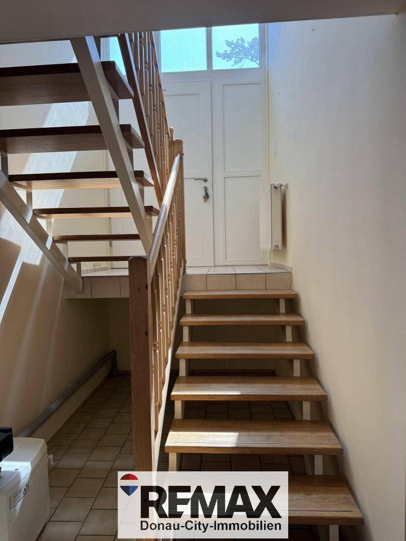 Helles Treppenhaus mit Holzstufen und Geländer, führt zu den oberen Etagen des Hauses.