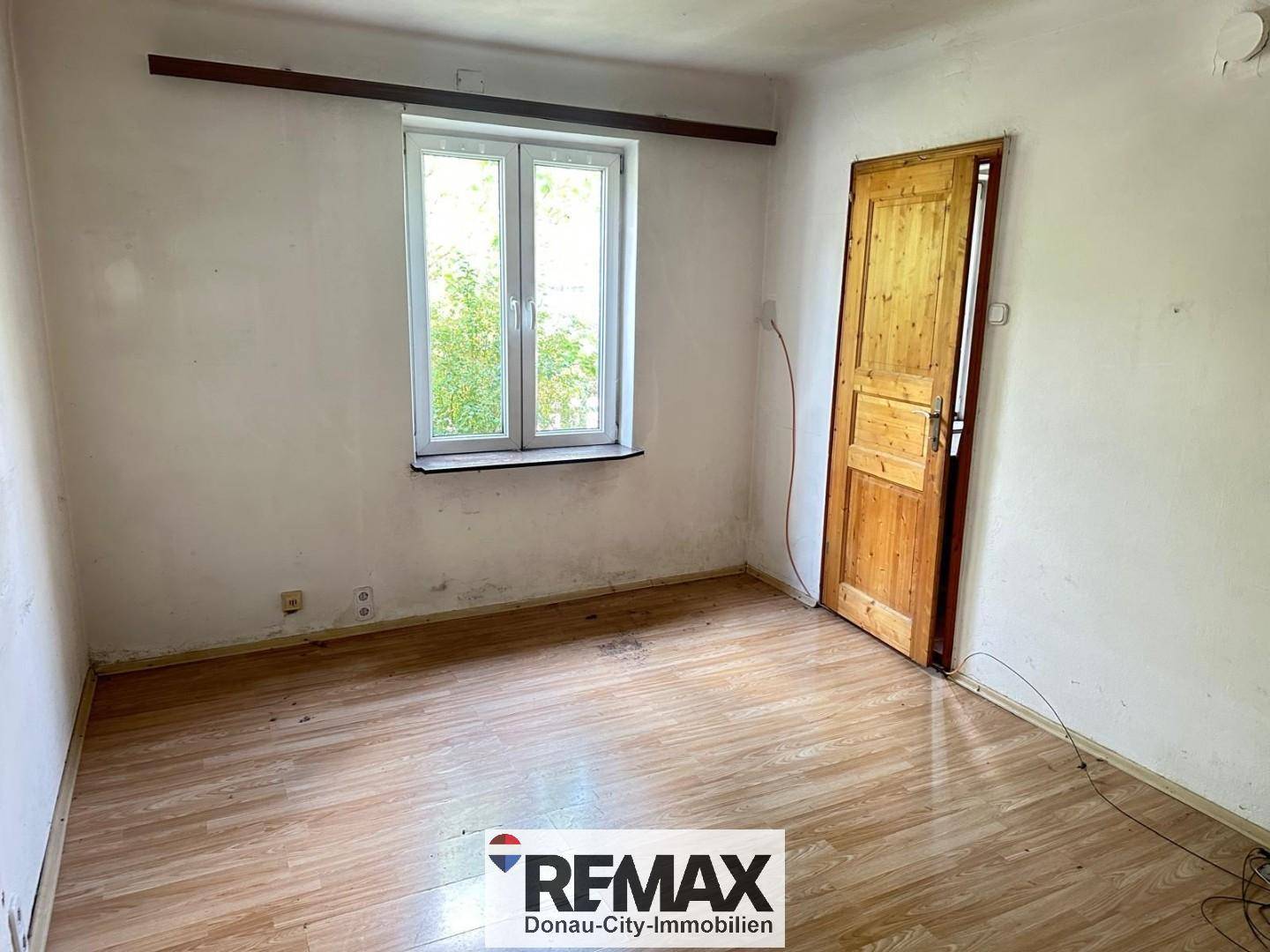 Leerer Raum mit abgenutzten Wänden, einem Fenster und einem Holzboden.
