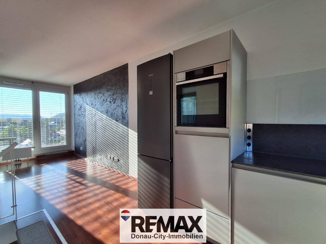 Moderne Küche mit integriertem Kühlschrank und Backofen, großen Fenstern und Laminatboden.