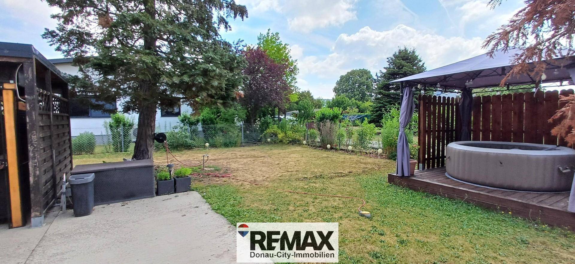 Großer Garten mit Rasenfläche, Bäumen und einem Whirlpool unter einem Pavillon.