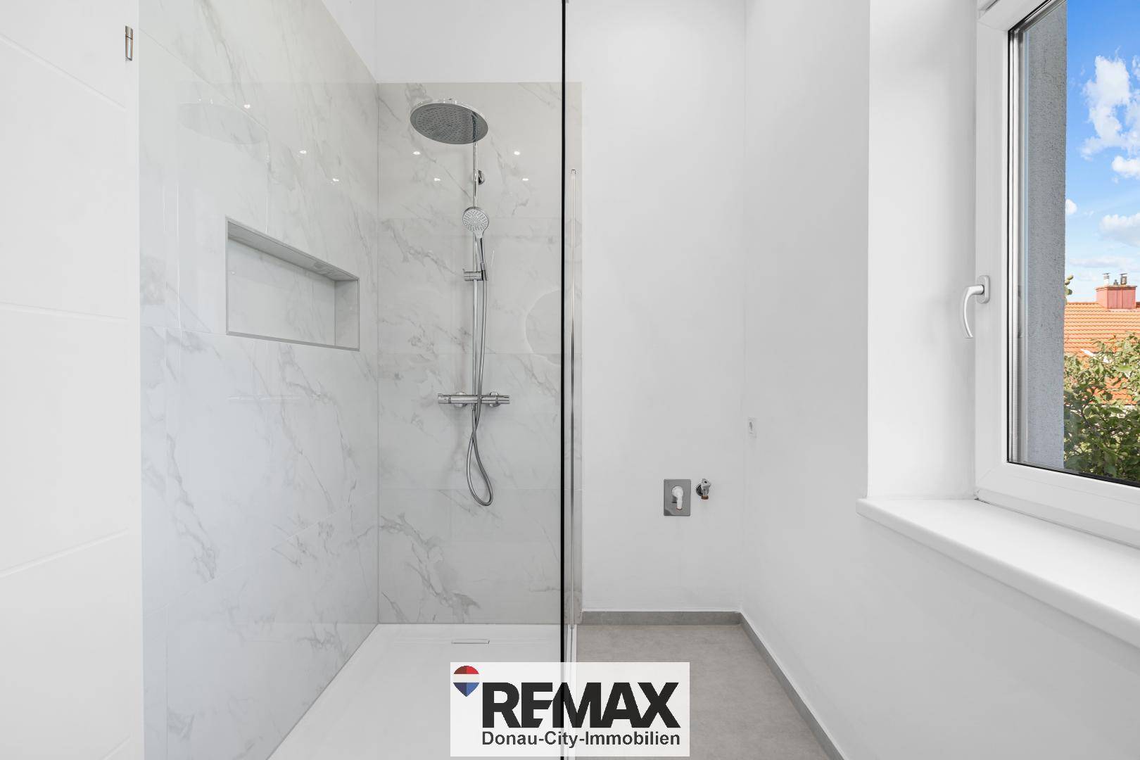 Helles Badezimmer mit großer begehbarer Dusche, Marmorfliesen und Fenster.