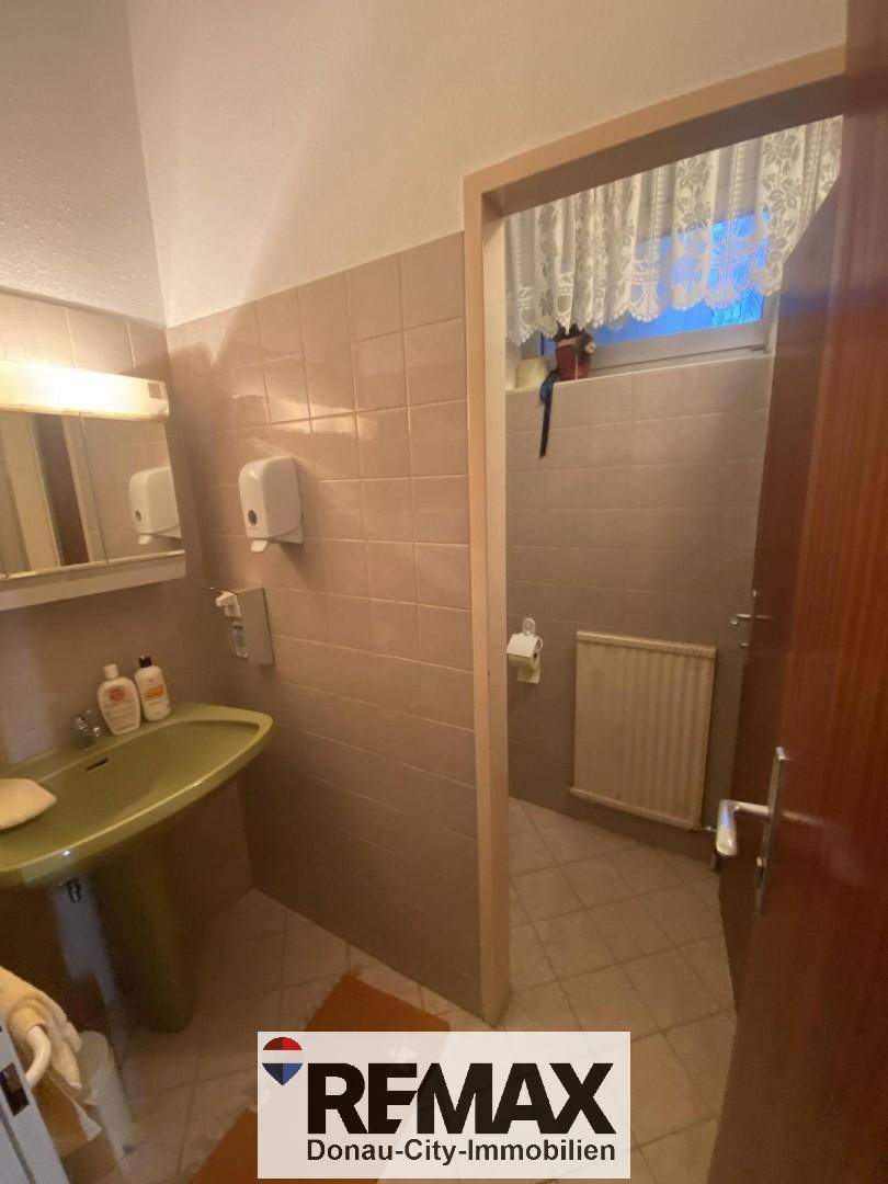 Badezimmer mit Waschbecken, Spiegel und Heizkörper, angrenzend an eine separate Toilette.