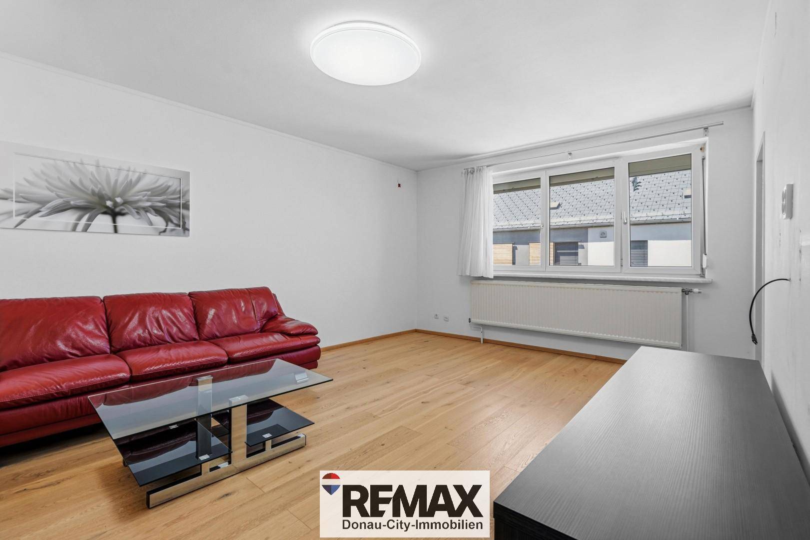 Helles Wohnzimmer mit großem Fenster, Heizkörper und rotem Ledersofa, bietet viel Tageslicht.