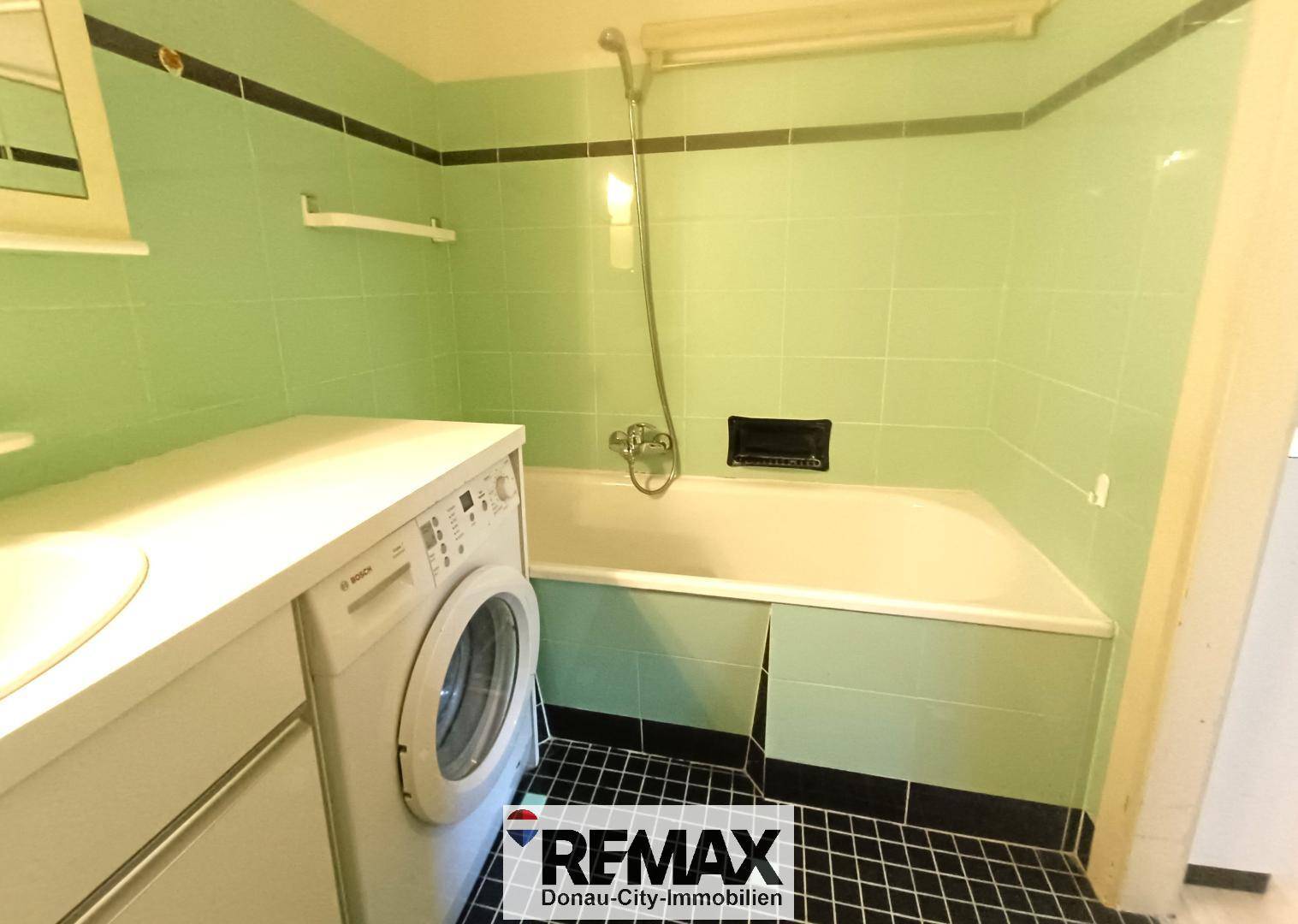Badezimmer mit grünen Wandfliesen, Badewanne und Duschvorrichtung.