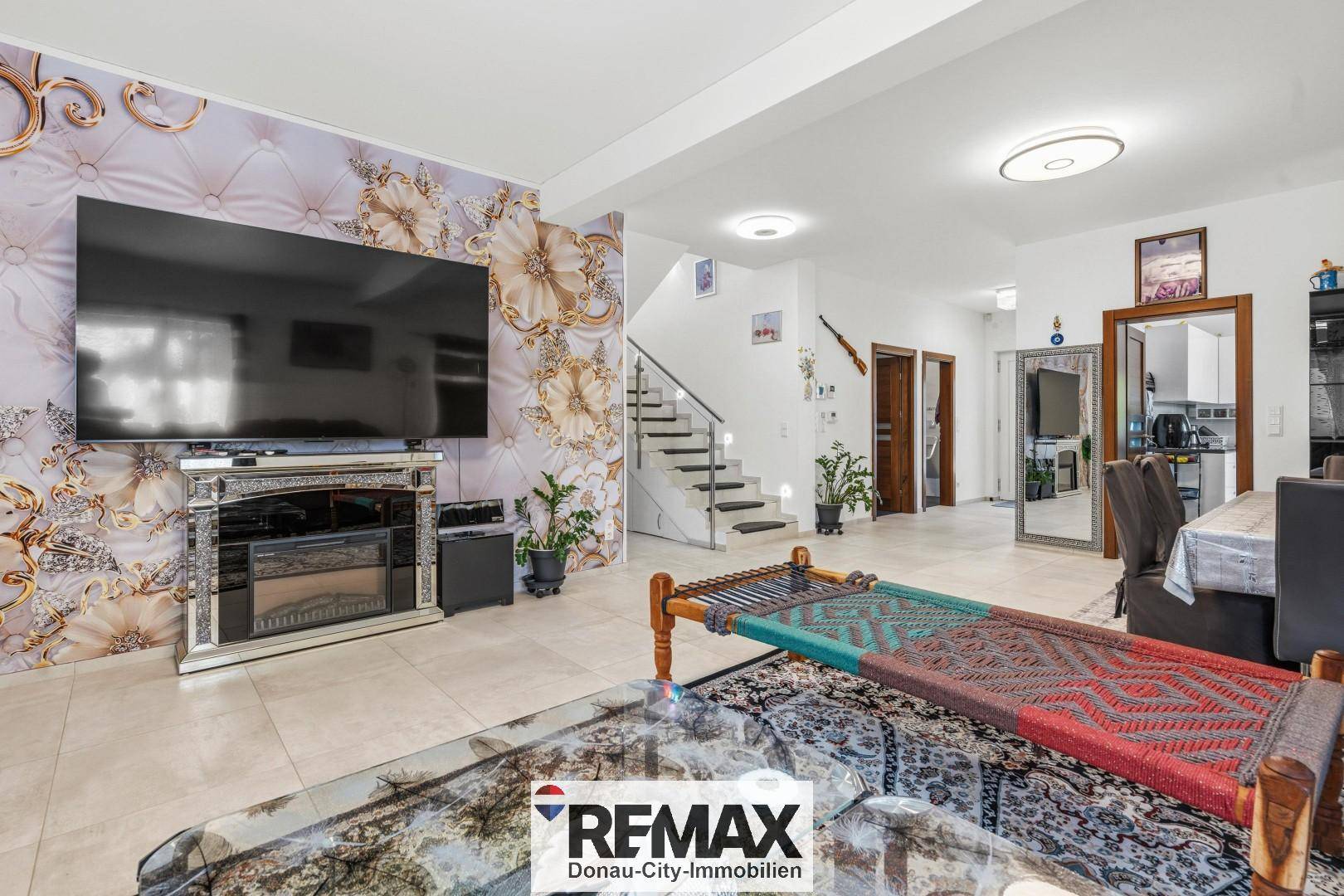 Modernes Wohnzimmer mit großem Fernseher, dekorativer Wandgestaltung und Zugang zur Treppe.