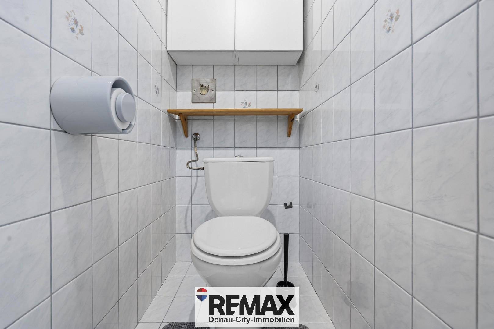Separates WC mit Fliesen an Wänden und Boden sowie einer kleinen Ablage.