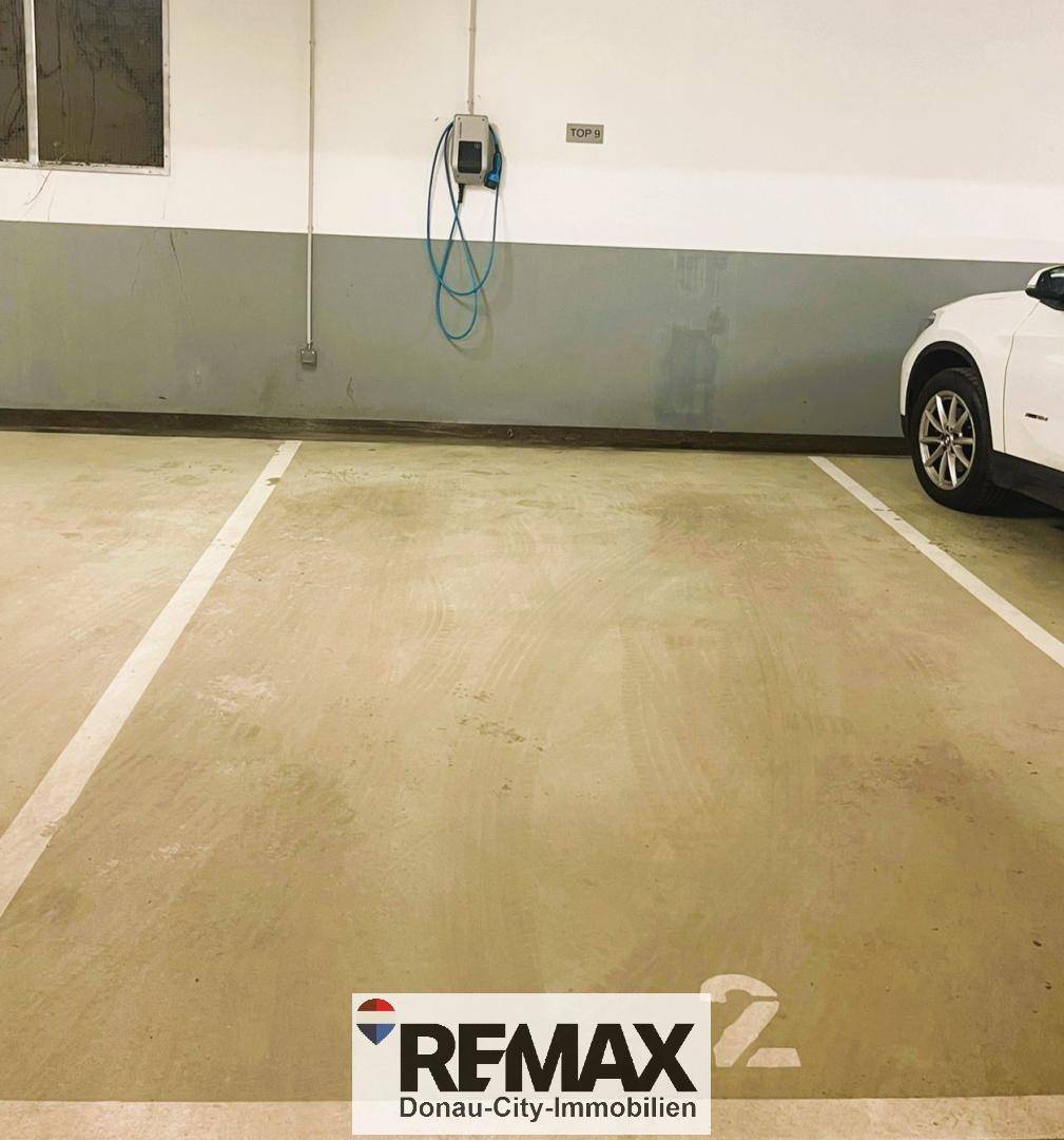 Tiefgaragenstellplatz mit klar markierten Linien und einer modernen Ladestation für Elektroautos.