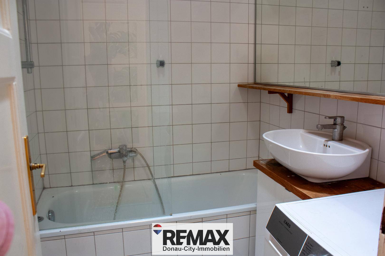 Badezimmer mit weißen Fliesen, Badewanne und einem modernen Aufsatzwaschbecken auf Holzablage.
