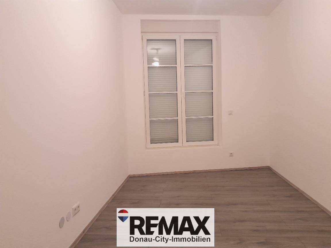 Unmöbliertes Zimmer mit hellem Laminatboden und großem Fenster, bereit zum Einzug.