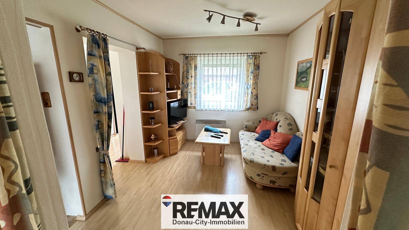 Gemütliches Wohnzimmer mit Sofa, Holzregalen und einem Fenster mit Vorhängen.