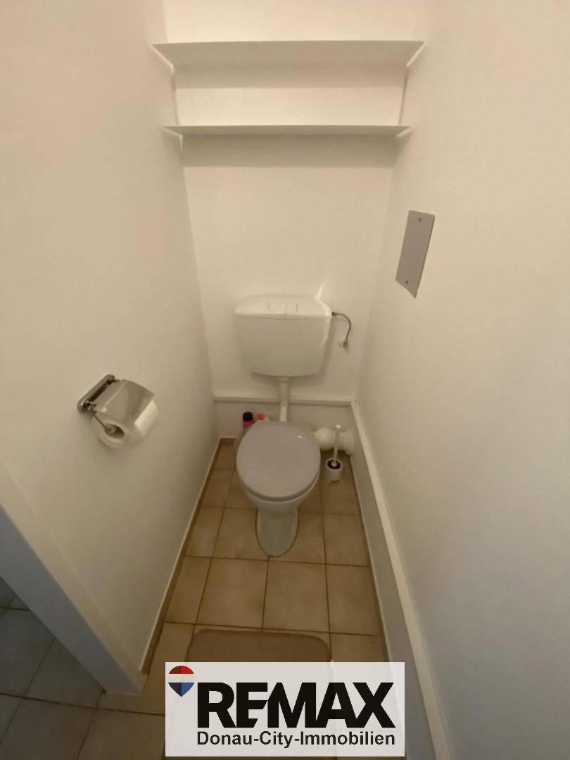Separate Toilette mit Fliesenboden und Wandregal, funktional und sauber.