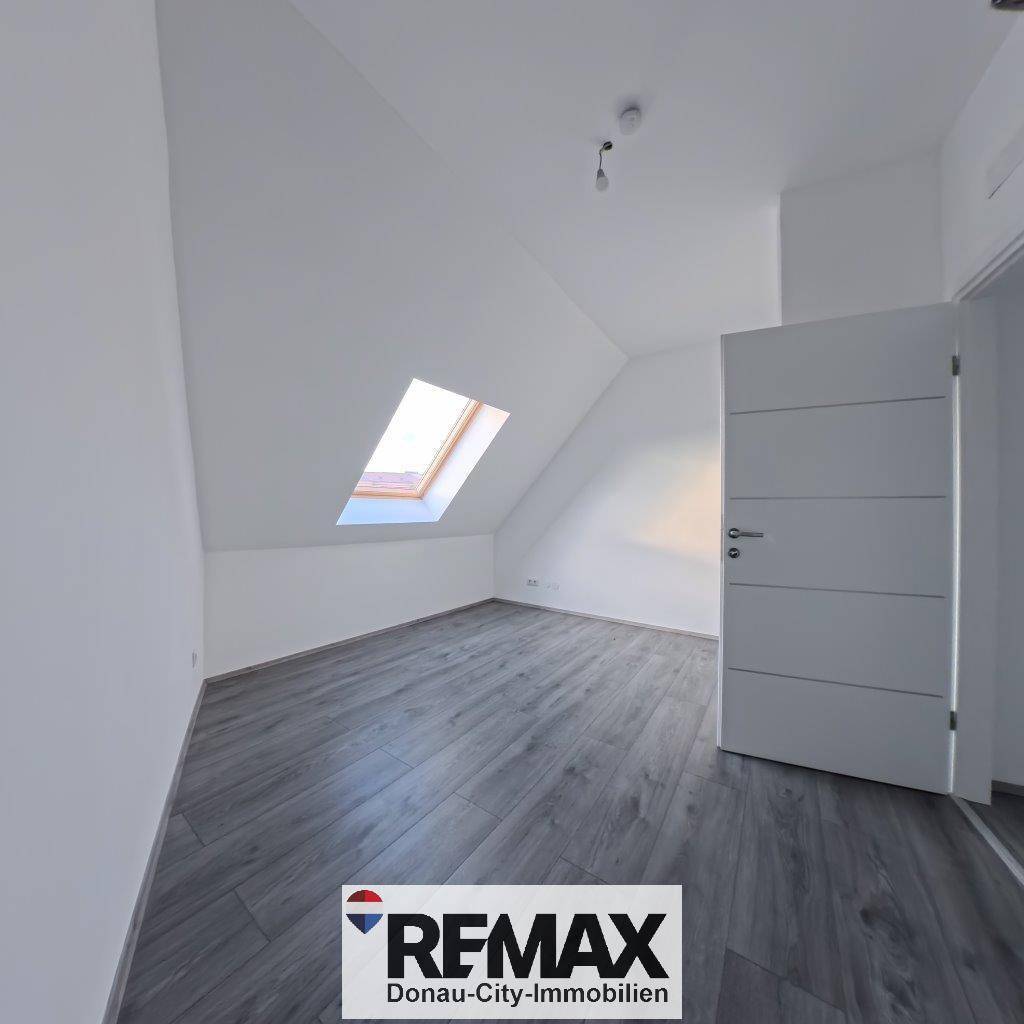 Helles Zimmer im Dachgeschoss mit Dachfenster, schrägen Wänden und Laminatboden.