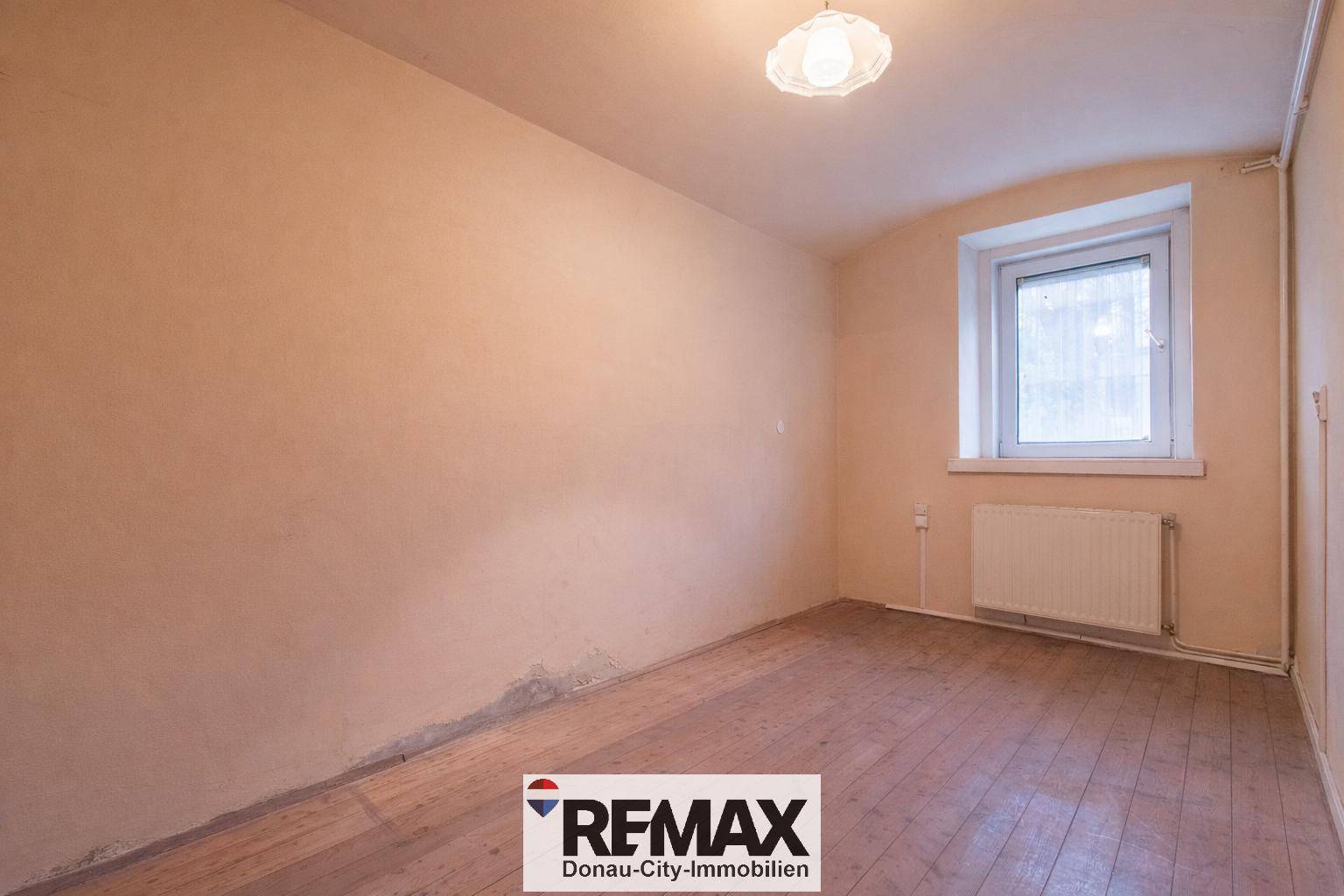 Leerer Raum mit beigen Wänden, Holzboden und Heizkörper unter einem Fenster.