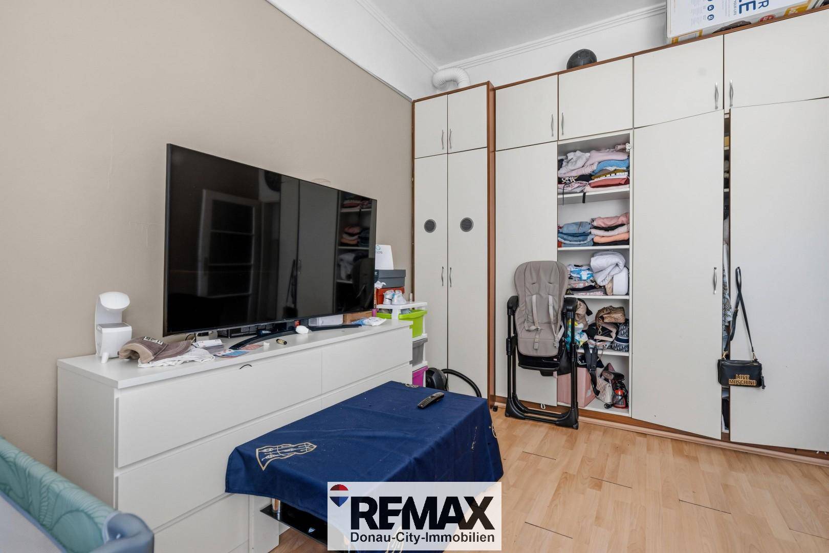 Schlafzimmer mit großem Fernseher, weißen Kommoden und praktischen Einbauschränken.