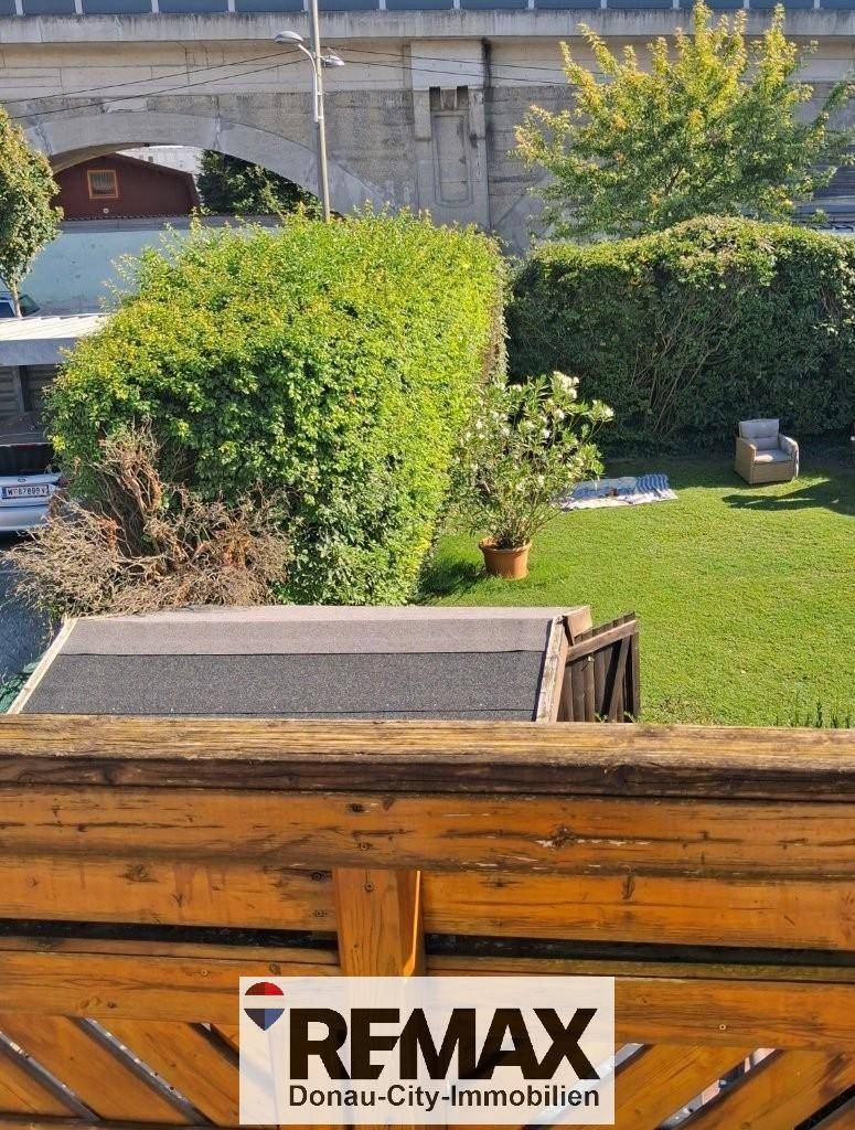 Blick von oben auf einen gepflegten Garten mit Rasenfläche, Gartenhaus und einer Brücke im Hintergrund.