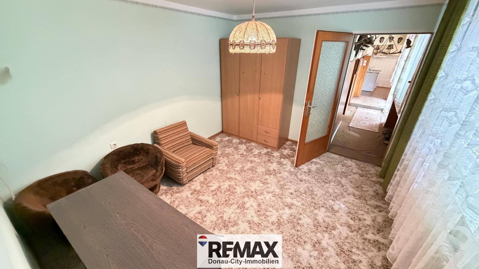 Zimmer mit Teppichboden, Kleiderschrank und einem Sessel, mit Blick in den Flur.