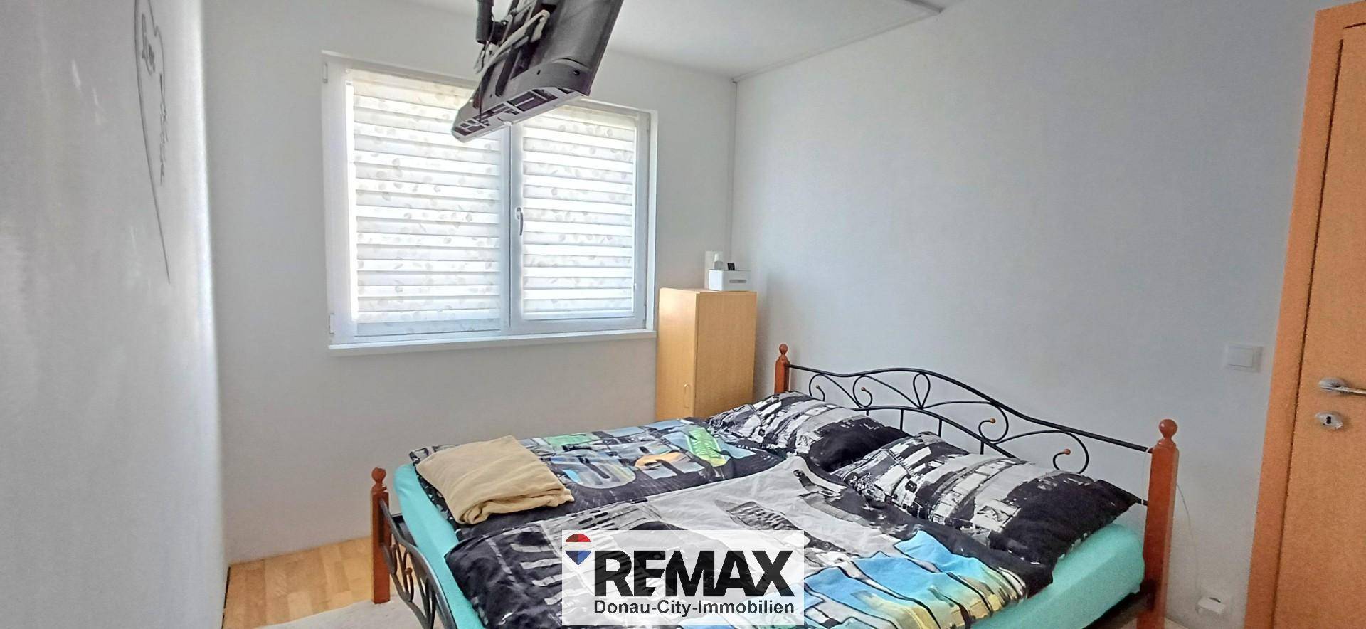 Schlafzimmer mit Doppelbett, Fenster mit Jalousien und schlichten Wänden.