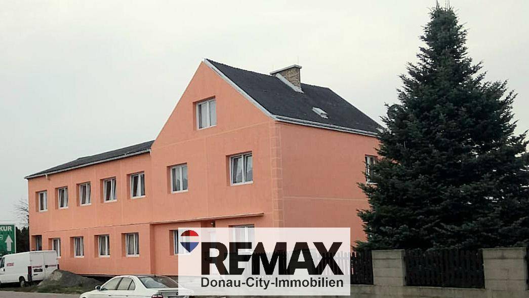Gebäude mit rosafarbener Fassade und mehreren Fenstern, umgeben von Bäumen.