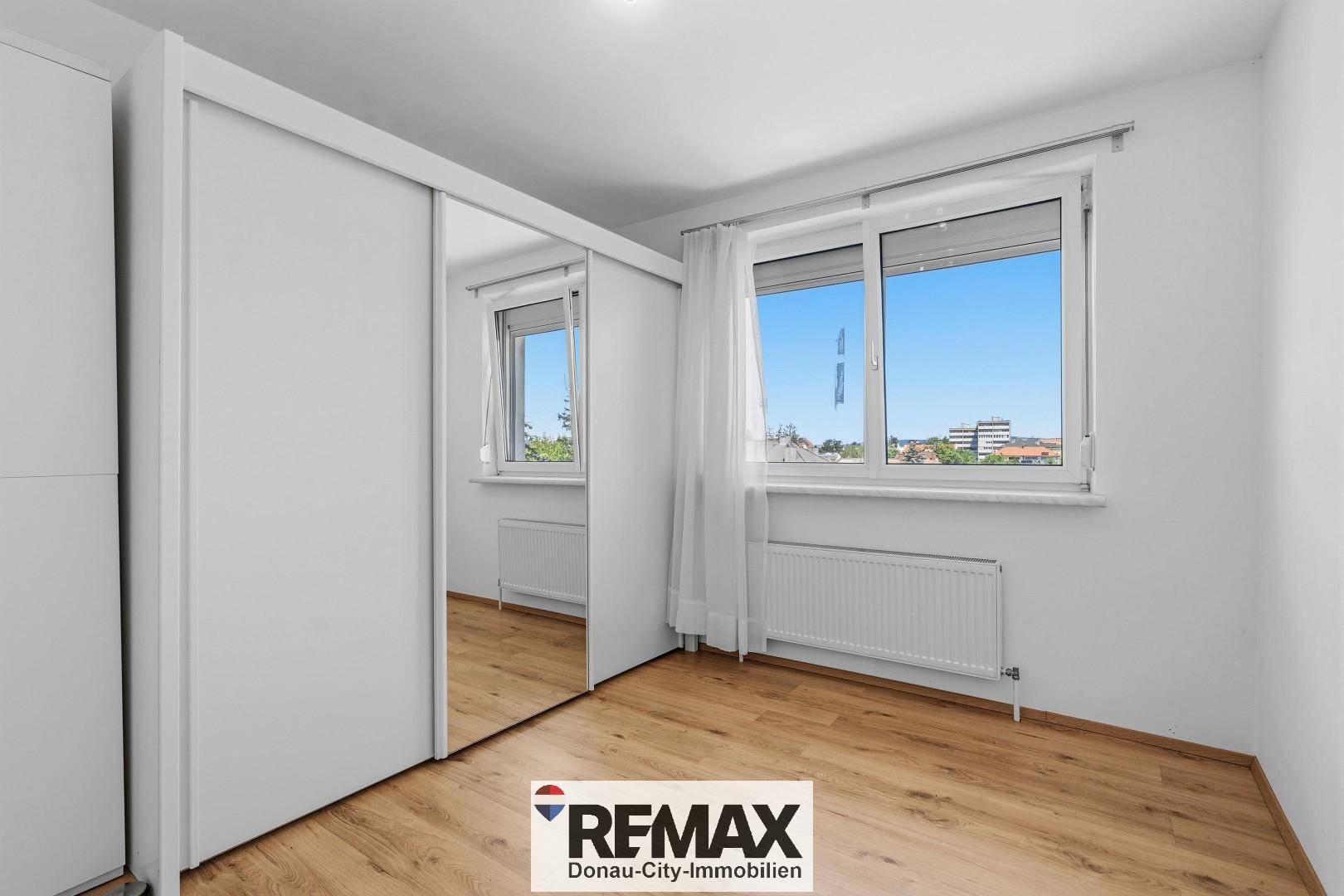 Geräumiges Schlafzimmer mit hellem Laminatboden und großem Spiegelschrank, bietet viel Stauraum.
