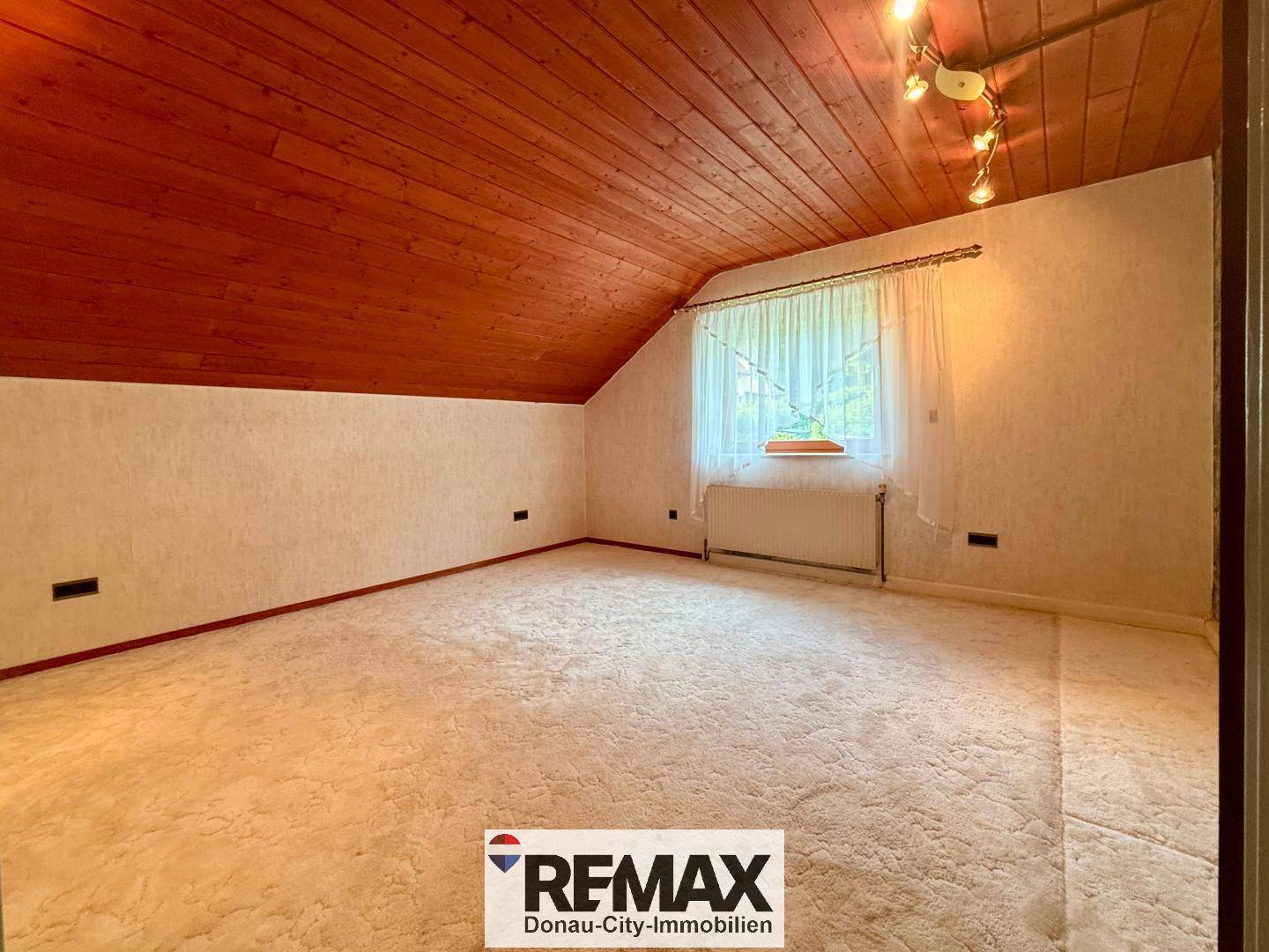 Helles Schlafzimmer im Dachgeschoss mit Holzdecke, beigem Teppichboden und Fenster.