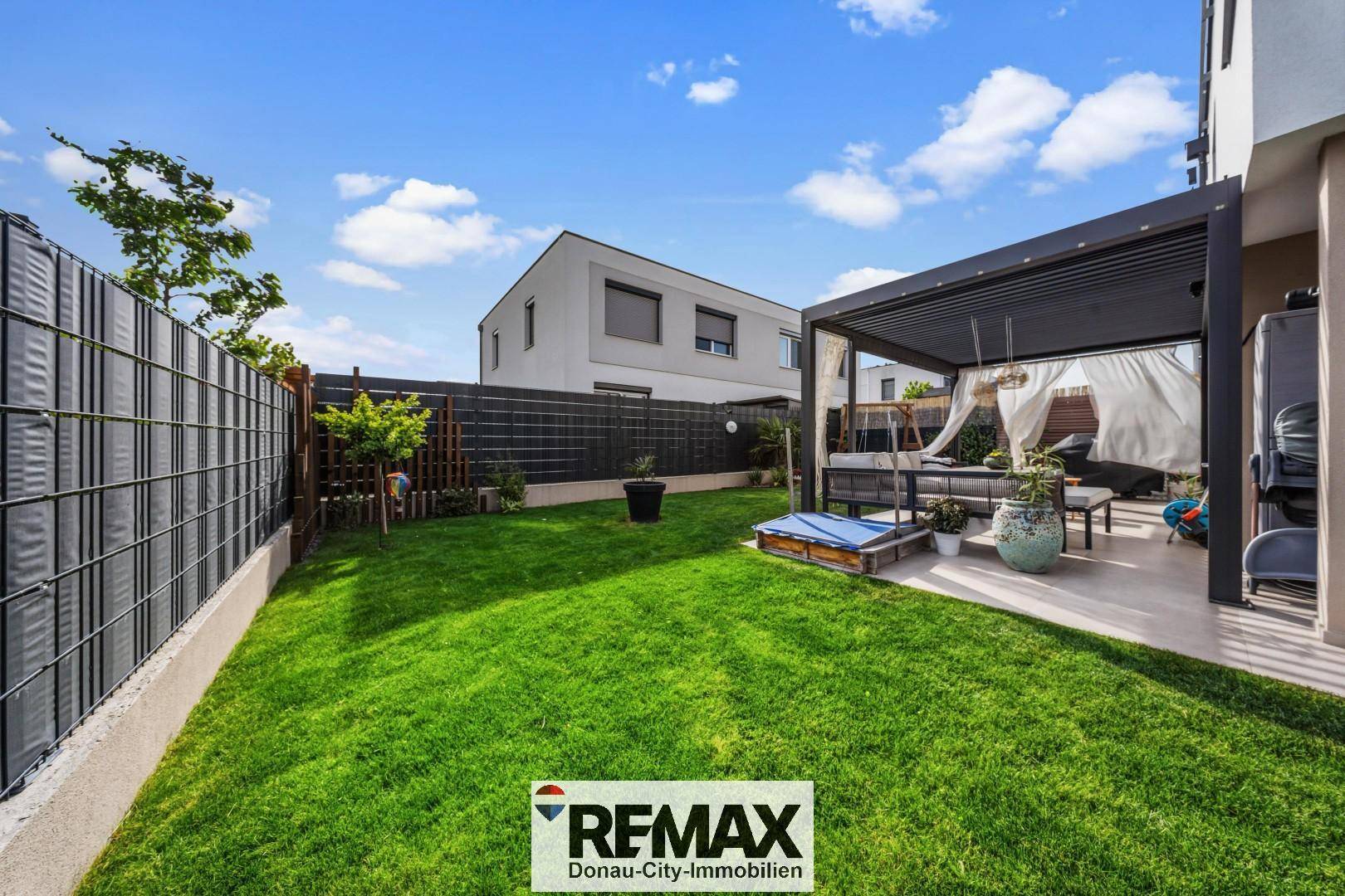 Gepflegter Garten mit Rasenfläche, Zaun und einer überdachten Terrasse, ideal zum Entspannen.