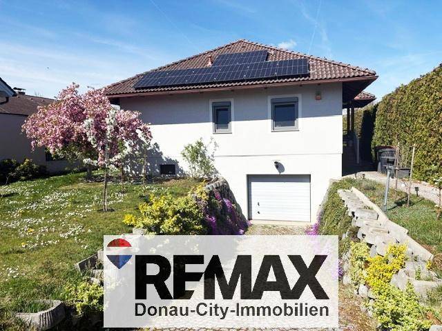 Ansicht des Hauses mit integrierter Garage, Solaranlage und blühenden Sträuchern im Vorgarten.