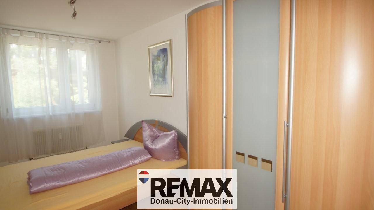 Schlafzimmer mit Bett, lila Bettwäsche und einem Kleiderschrank mit Holzelementen und Milchglas.