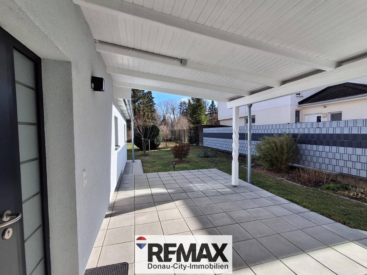 Überdachte Terrasse mit hellen Fliesen und Zugang zum Gartenbereich des Hauses.