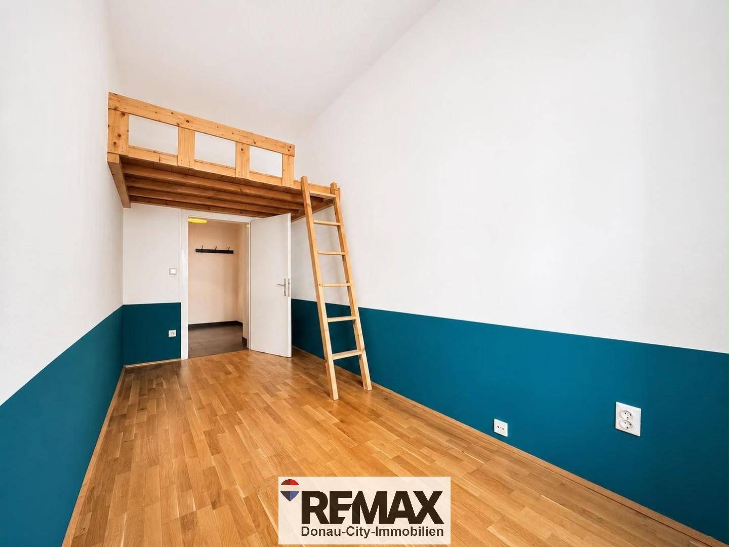 Freundliches Zimmer mit Holzboden, blauer Akzentwand und Hochbettkonstruktion aus Holz.