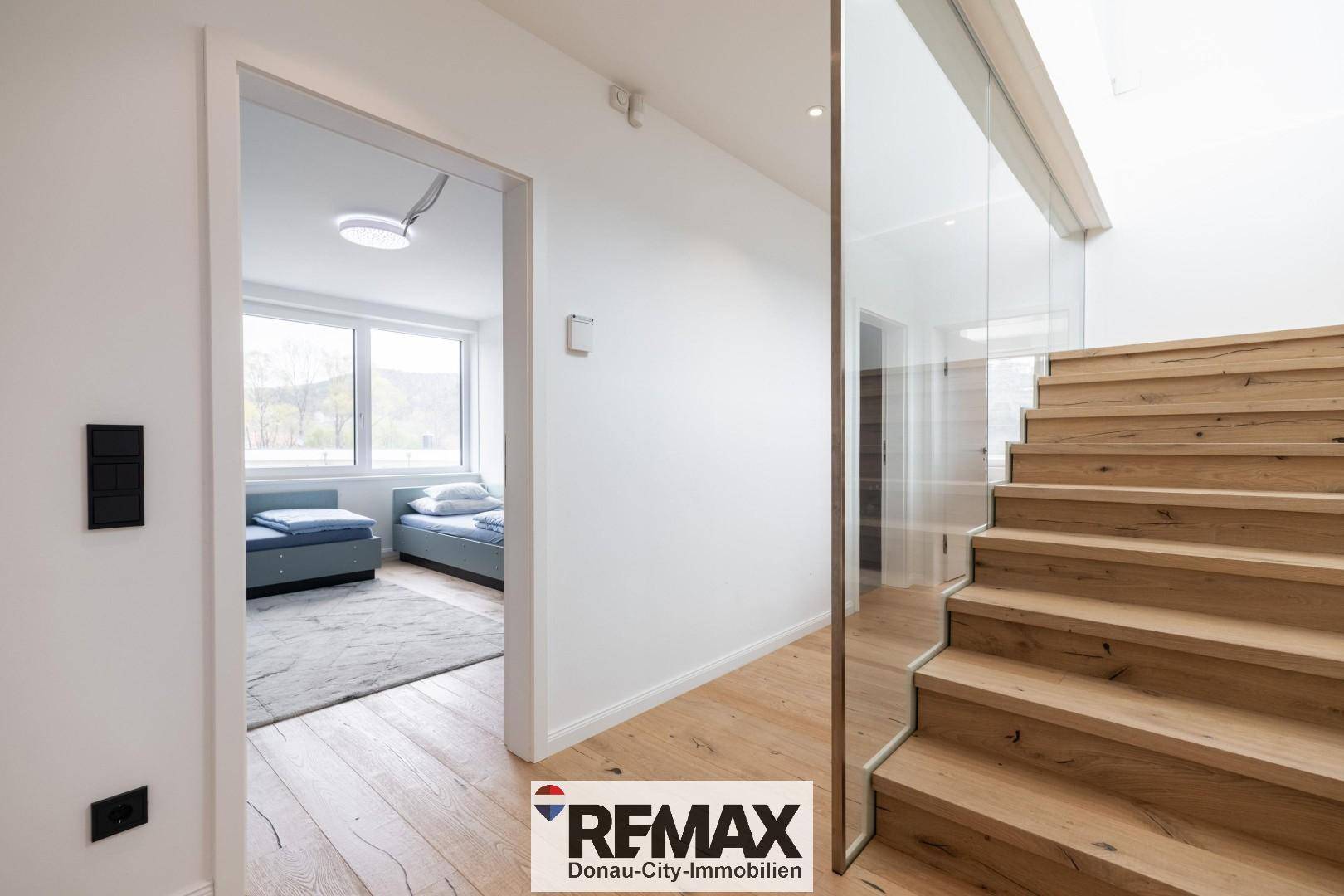 Heller Flur mit Holztreppe und Blick in ein angrenzendes Schlafzimmer.