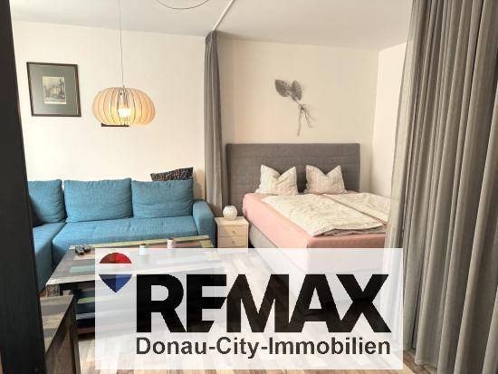 Gemütlicher Wohnbereich mit blauem Ecksofa und einem durch Vorhang abgetrennten Schlafbereich.
