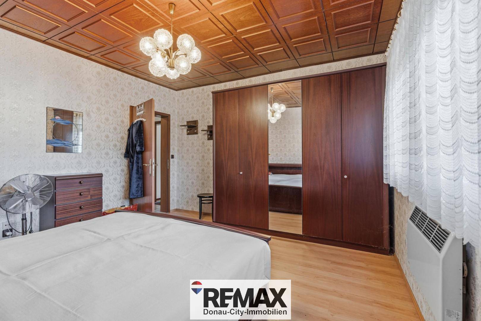Schlafzimmer mit Holzfußboden, großem Kleiderschrank und gemusterter Tapete.