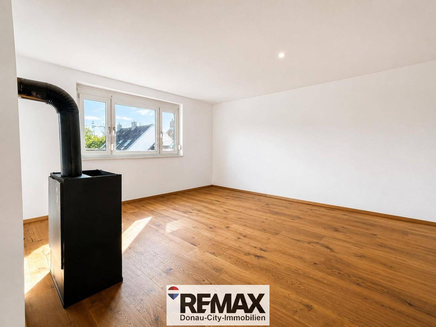 Heller Raum mit Holzboden und einem stilvollen Holzofen, ideal als zukünftiges Wohnzimmer.