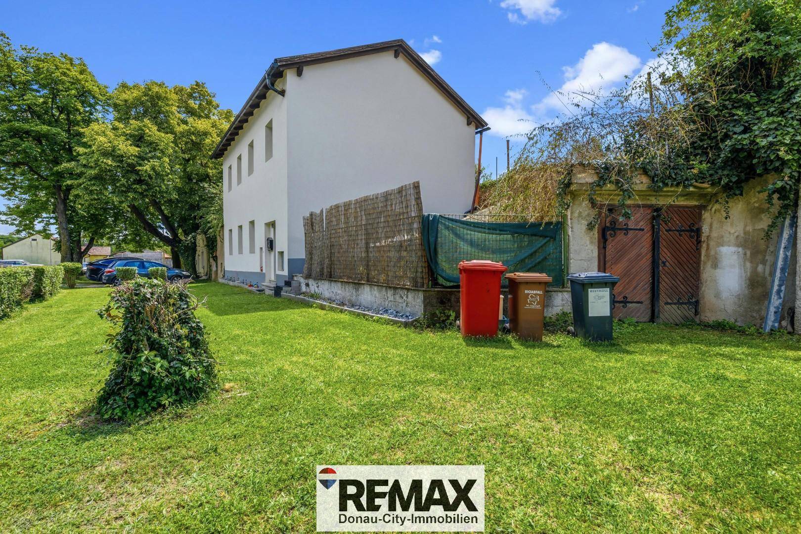 Seitenansicht des Hauses mit großem Rasenbereich und alten Mauern im Hintergrund.