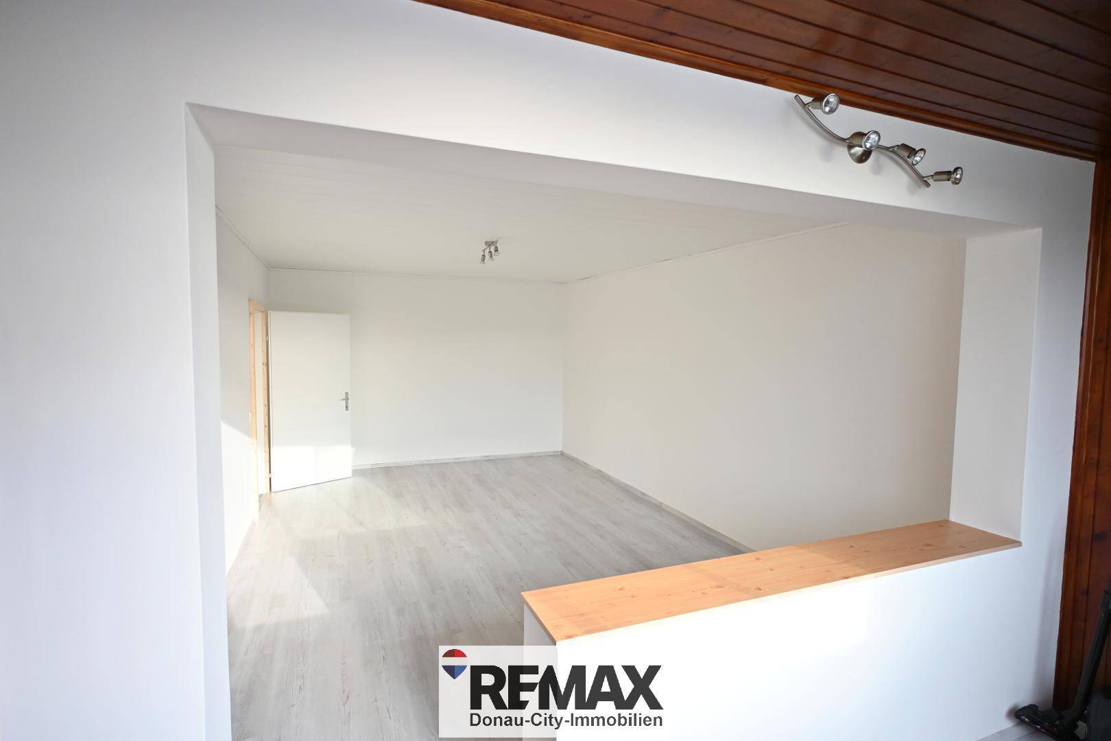 Offener Wohnbereich mit hellem Laminatboden und einer Holzdecke, die Gemütlichkeit verleiht.